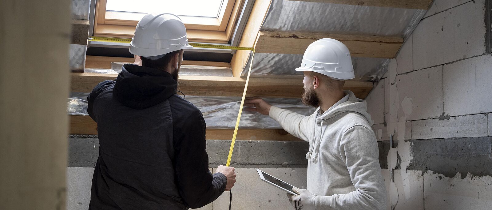 Menschen mit Helmen die sich prüfend die Wände in einem Rohbau ansehen.