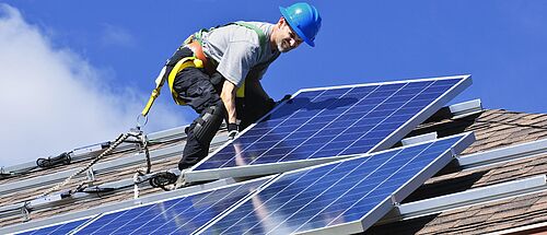 Ein Baufacharbeiter steht auf dem Dach eines Hauses und legt eine weiteres Solarpanel an.