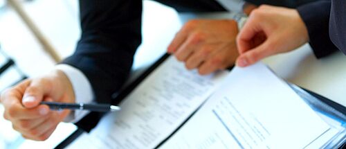 Zwei Personen sehen sich am Schreibtisch Unterlagen an, beraten dazu und machen sich Notizen