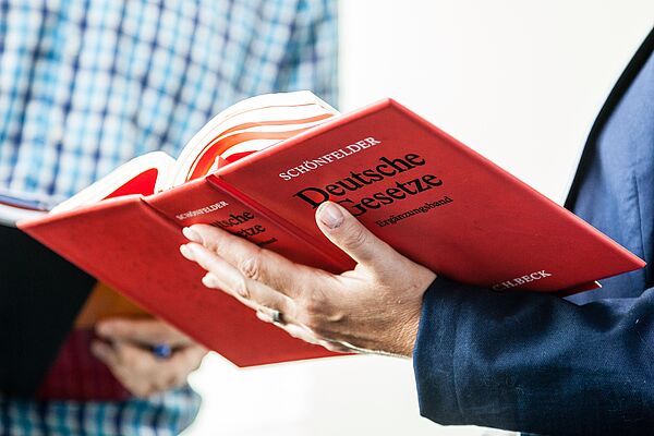 Eine Person blättert im Buch \"Deutsche Gesetzte\" eine nebenstehende Person schaut mit rein.