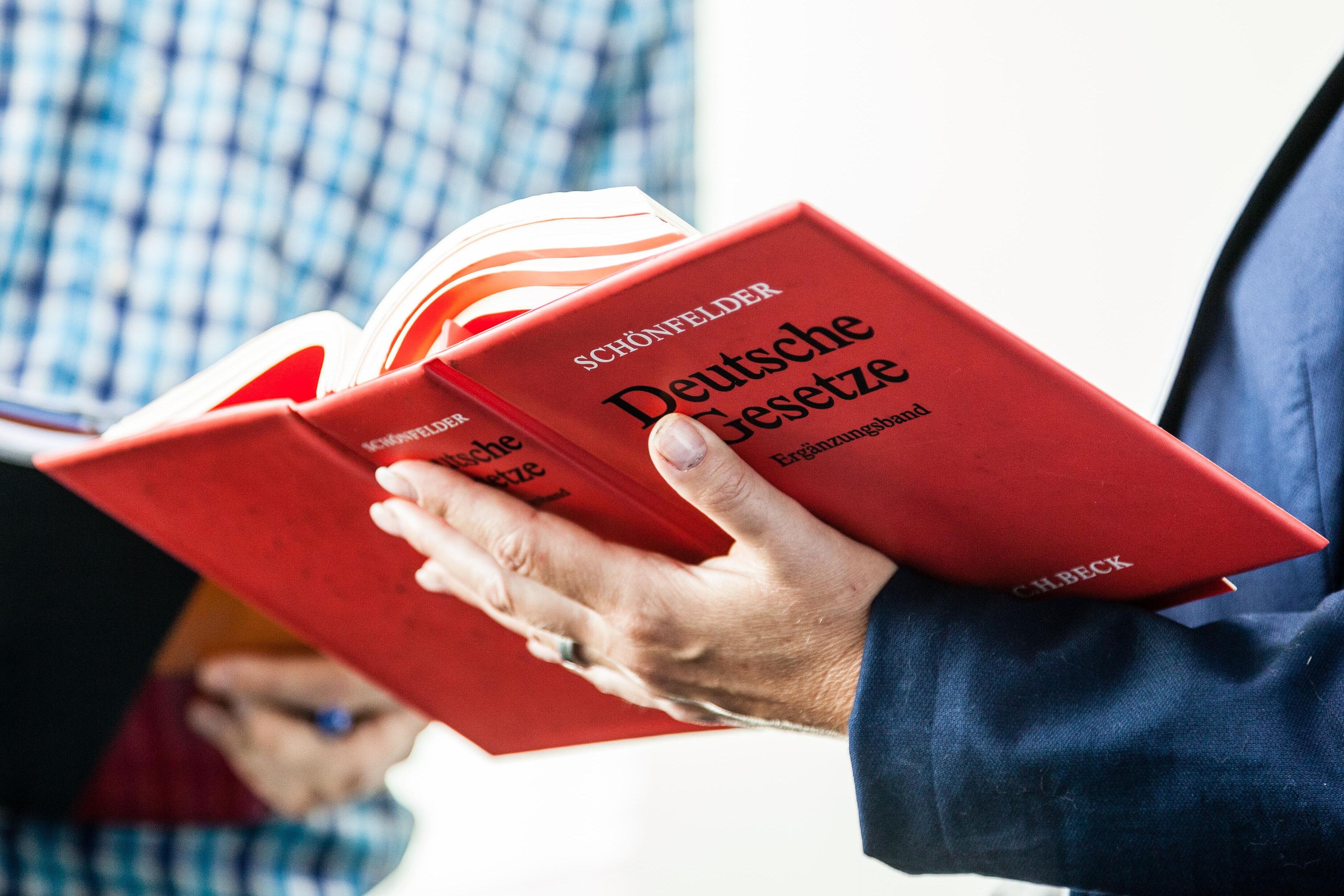 Eine Person blättert im Buch \"Deutsche Gesetzte\" eine nebenstehende Person schaut mit rein.