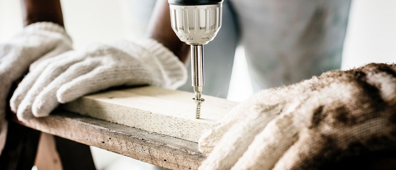 Eine Person arbeitet mit einem Bohrer an einem Holzwerkstück, links und rechts halten weitere Personen das Werkstück fest.