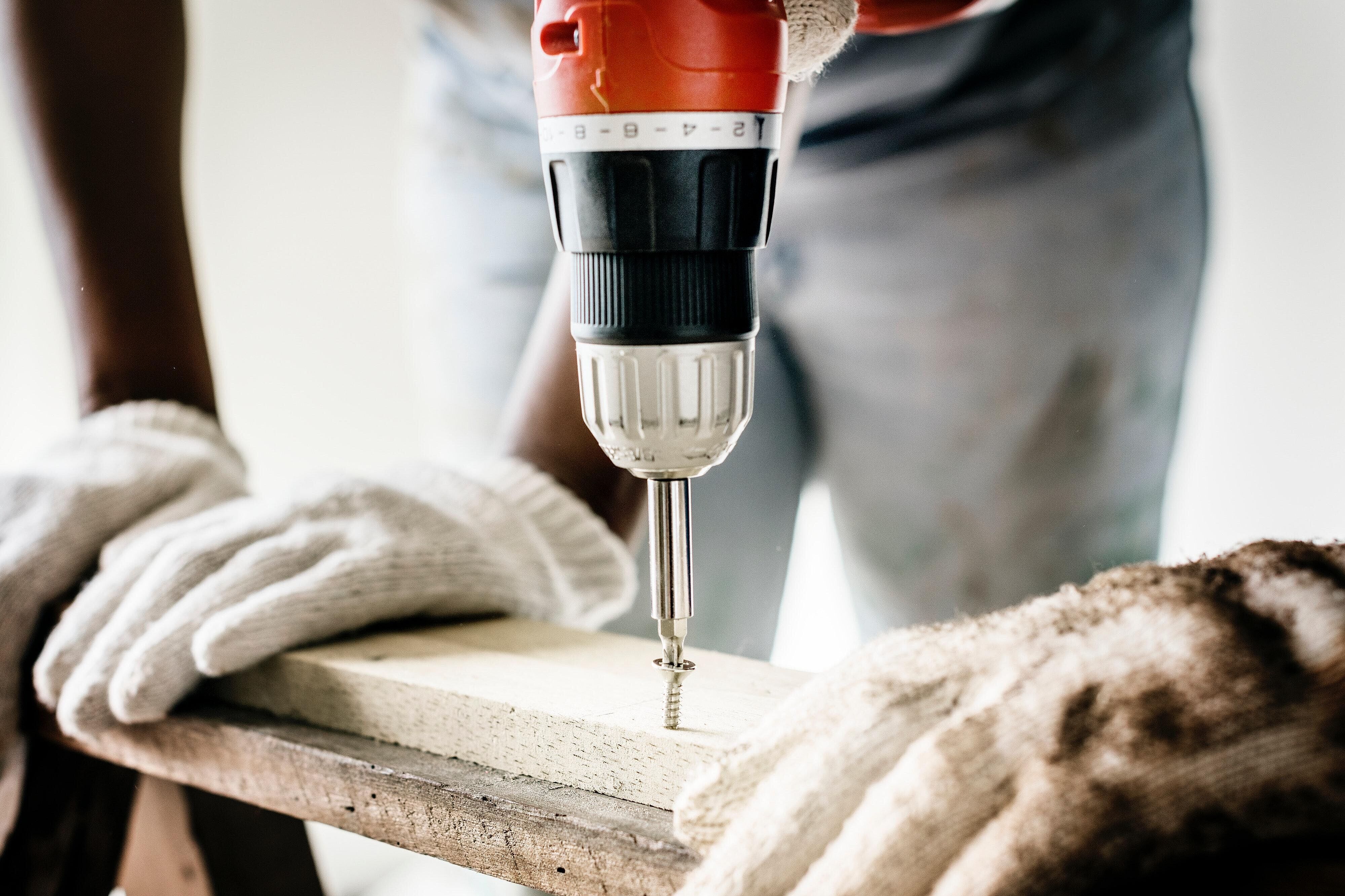 Eine Person arbeitet mit einem Bohrer an einem Holzwerkstück, links und rechts halten weitere Personen das Werkstück fest.