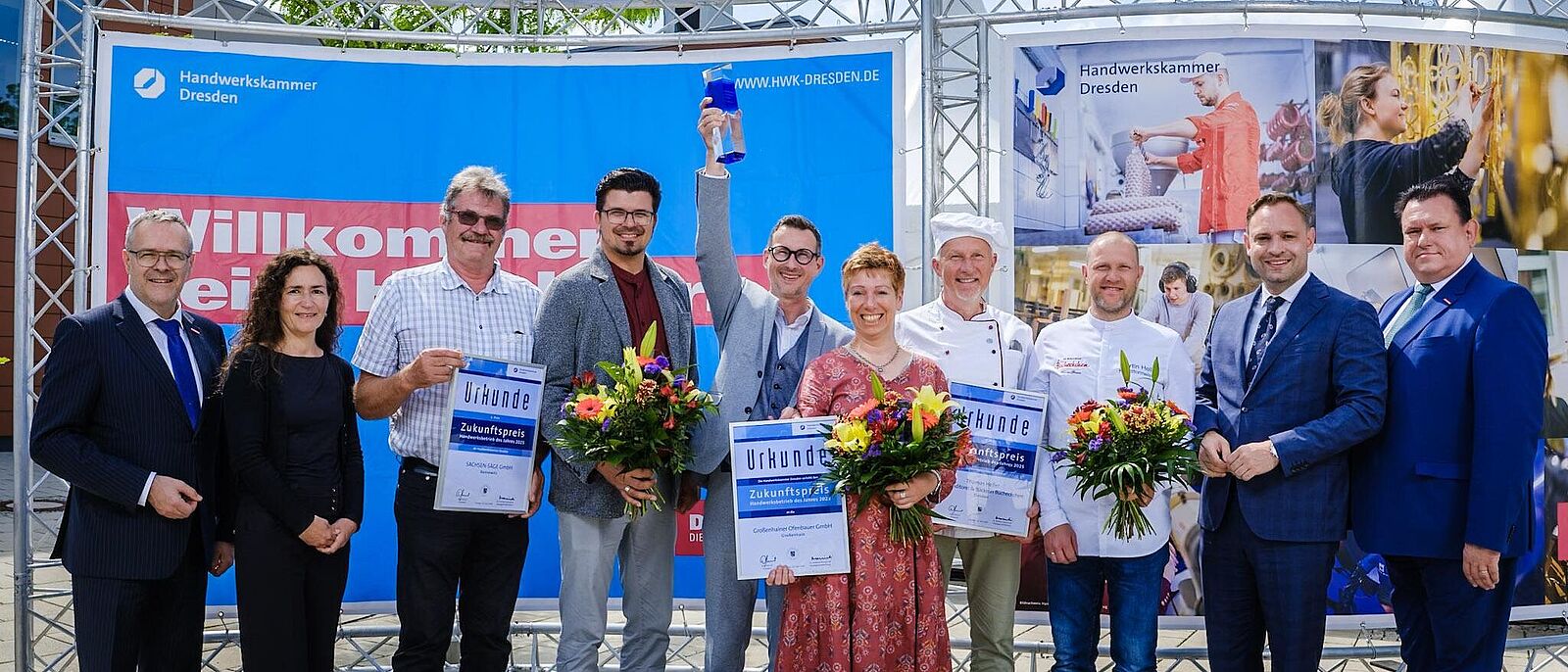 Die Gewinner des Zukunftspreises 2025 der ersten drei Plätze werden gemeinsam auf der Bühne geehrt und halten Urkunden sowie Blumensträuße in den Händen.