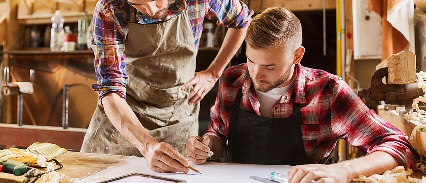 Zwei Handwerker am Werktisch - Zum Beitrag