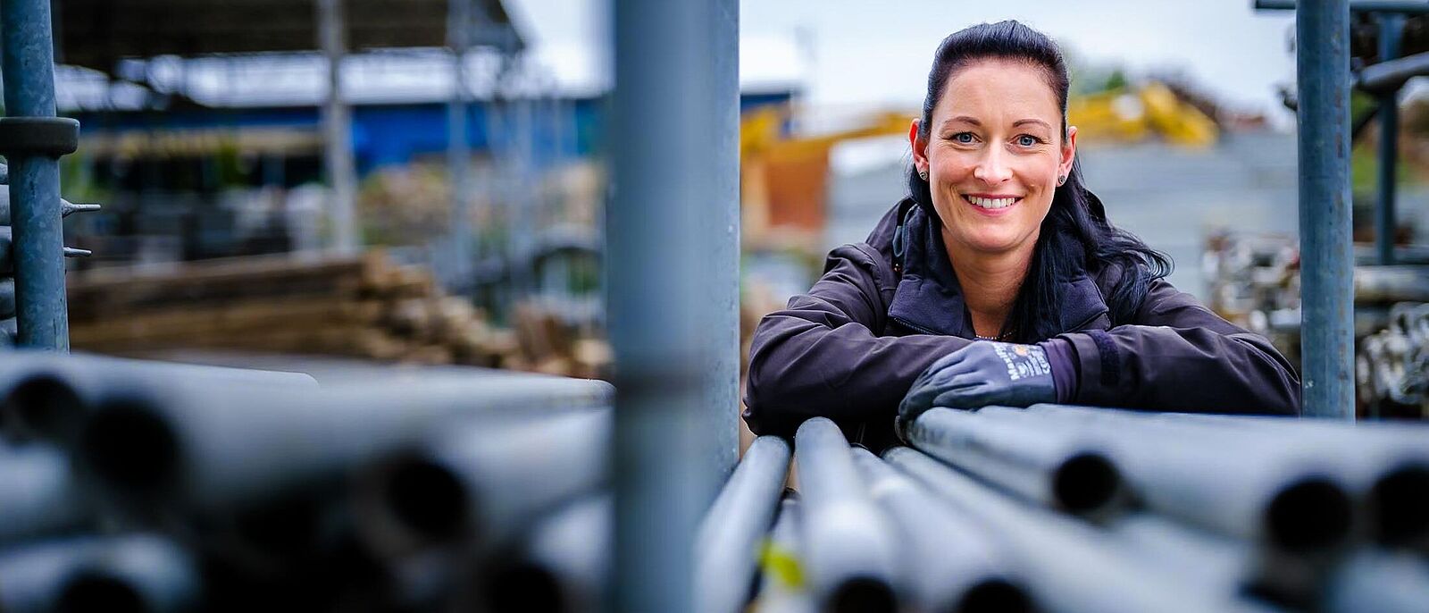 Eine weibliche Person stützt sich auf einen Stabel mit Gerüstelementen.