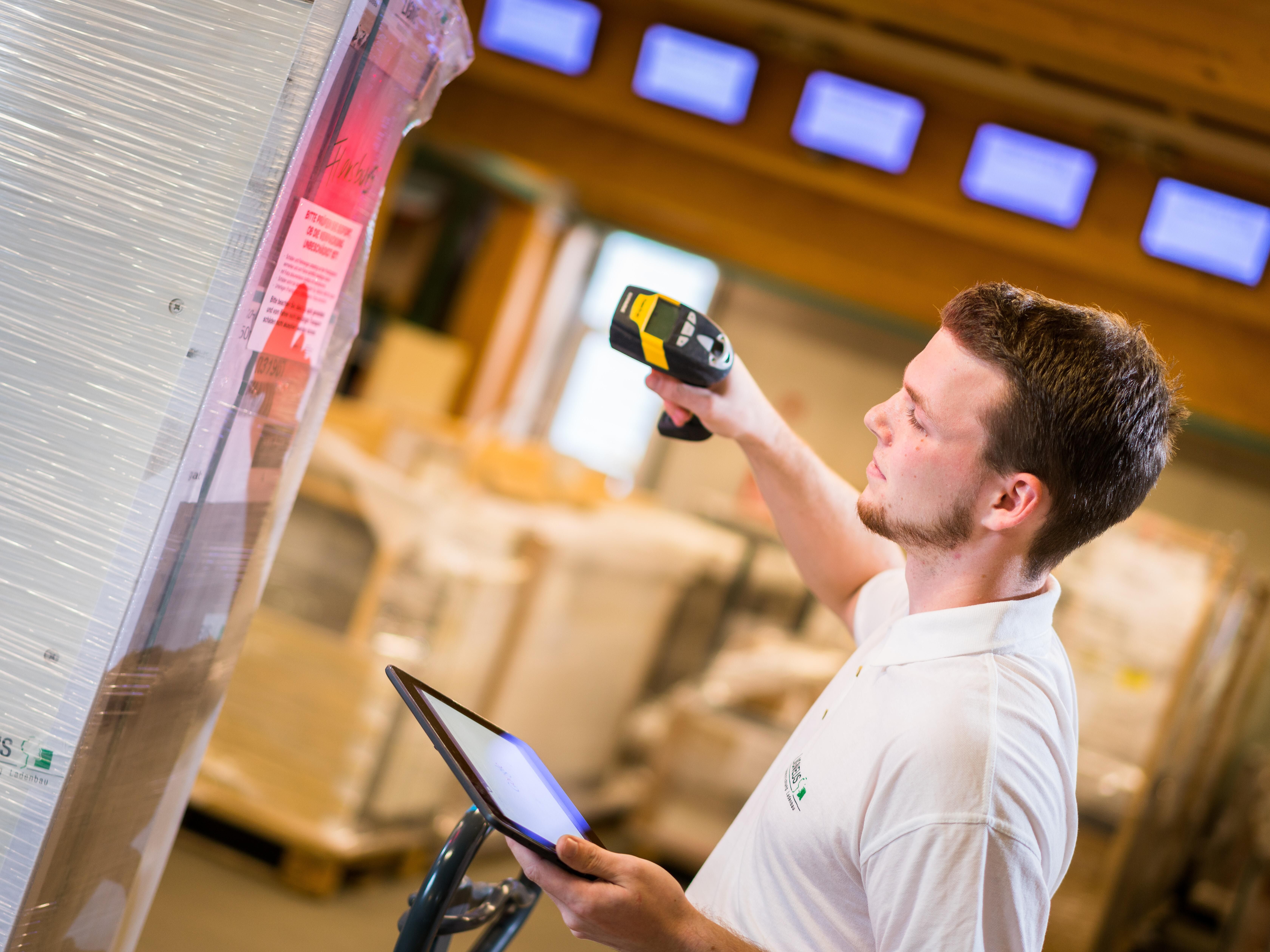 Eine Person steht vor einem Lageregal und scannt/digitalisiert ein Produkt.