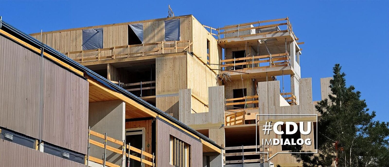 blick auf einen Rohbau eines teilweise holzverkleideten Gebäudekomplexes.