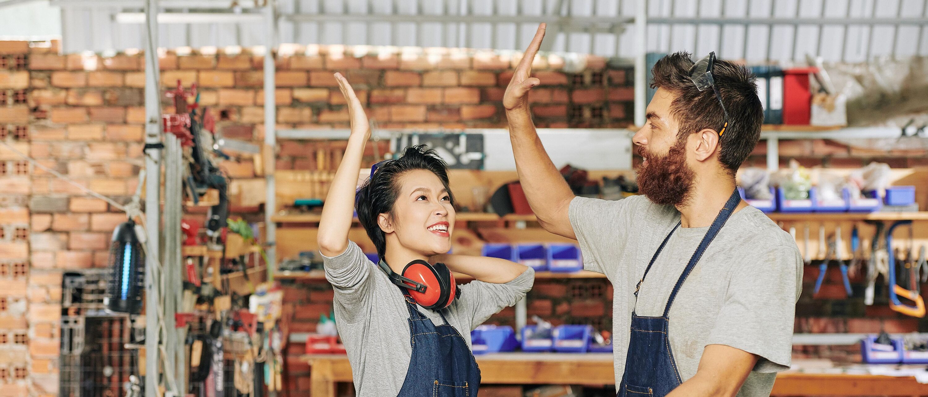 Zwei Personen stehen in einer Tischlerwerkstatt und geben sich \"high five\".