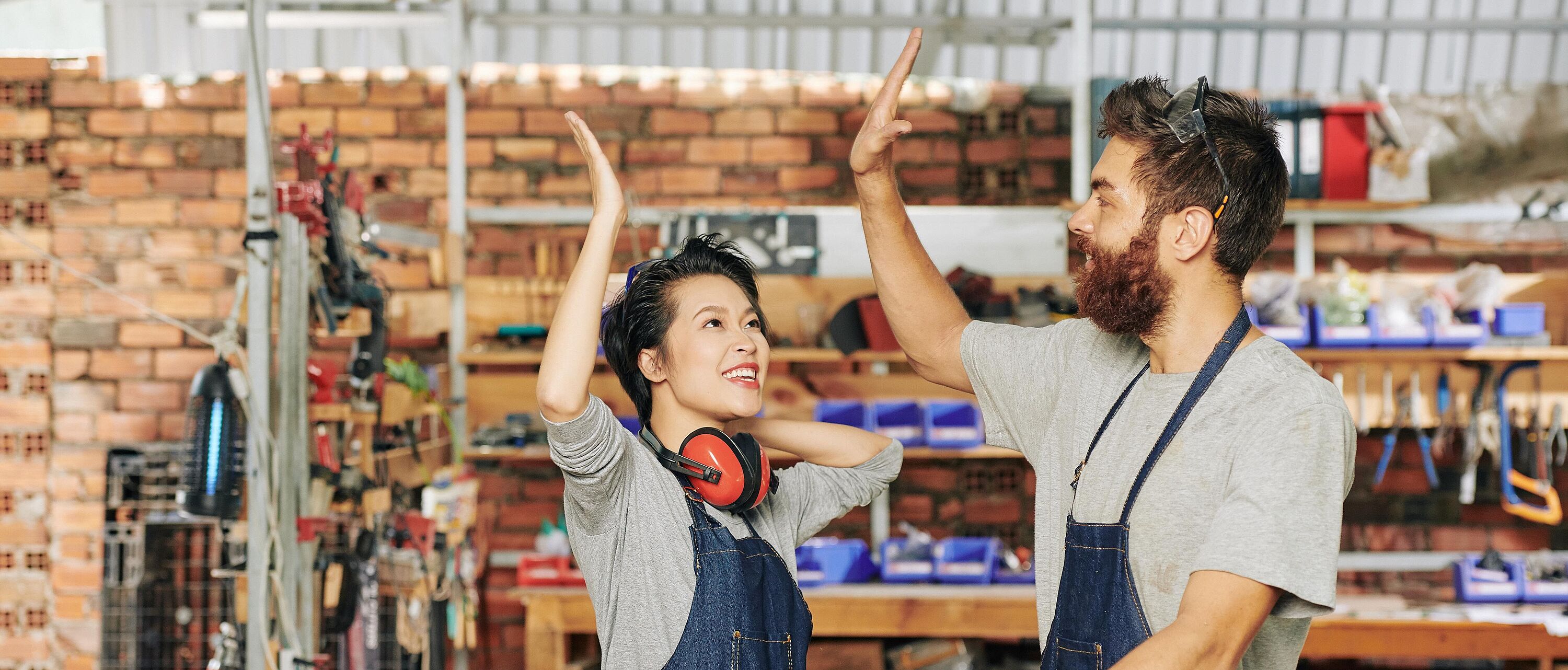 Zwei Personen stehen in einer Tischlerwerkstatt und geben sich \"high five\".