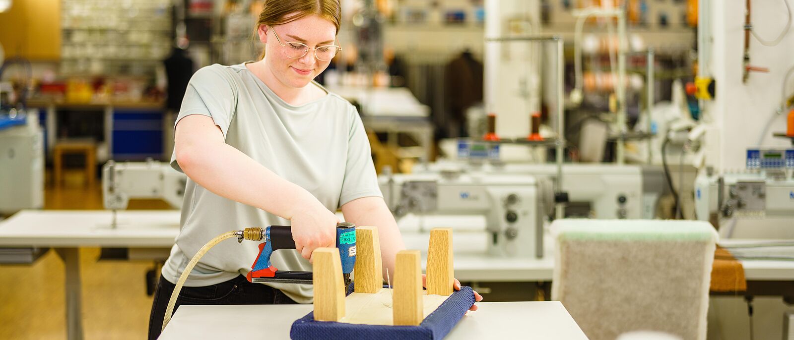 Für  die Herstellung des Junior-Meisterstücks befestigt Alisa N. blauen Stoff an einen Holzhocker mit einem Elektrotacker.