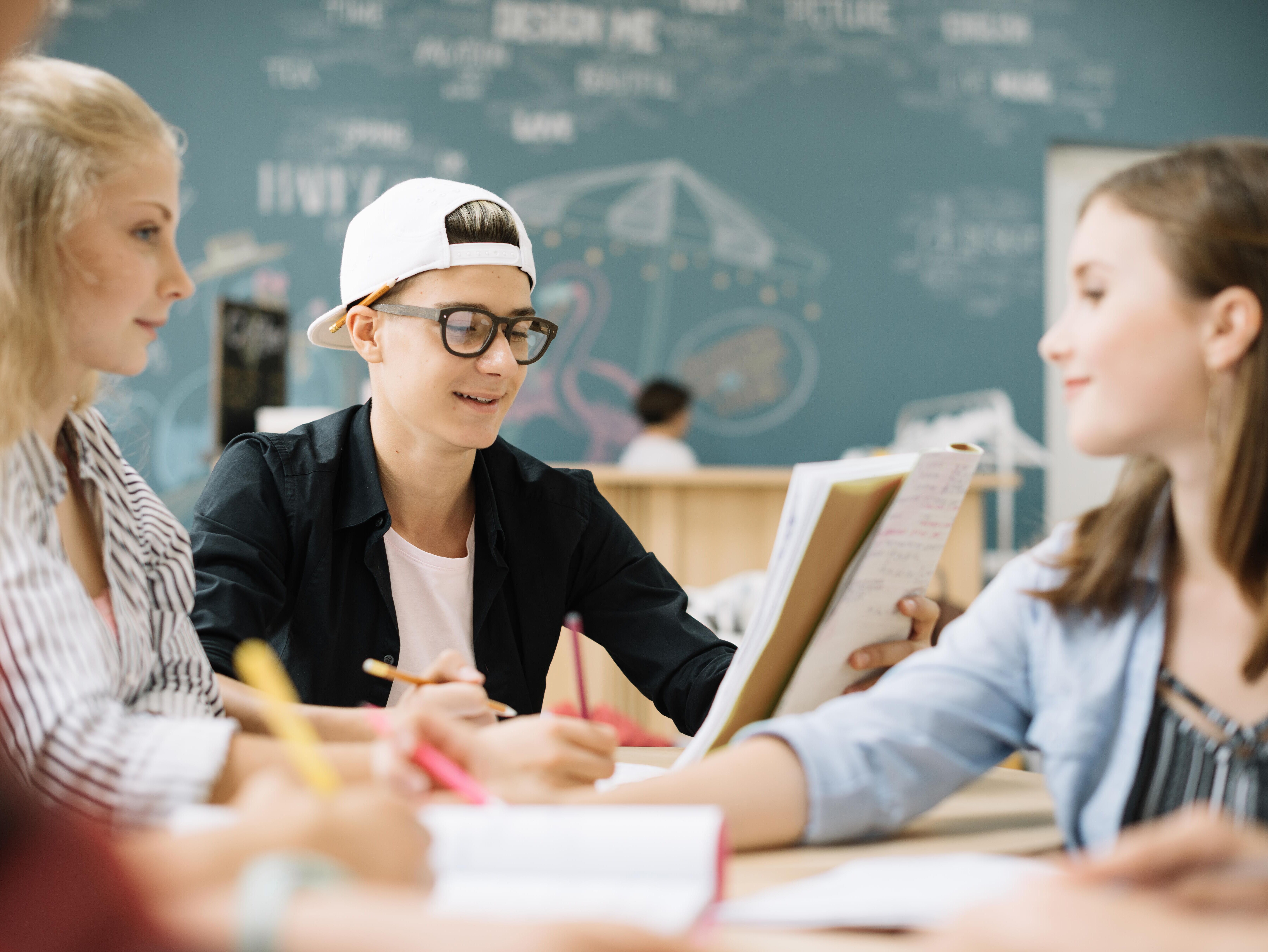 § Schüler sitzen gemeinsam am Tisch und lösen Aufgaben im Hintergrund eine Kreidetafel.