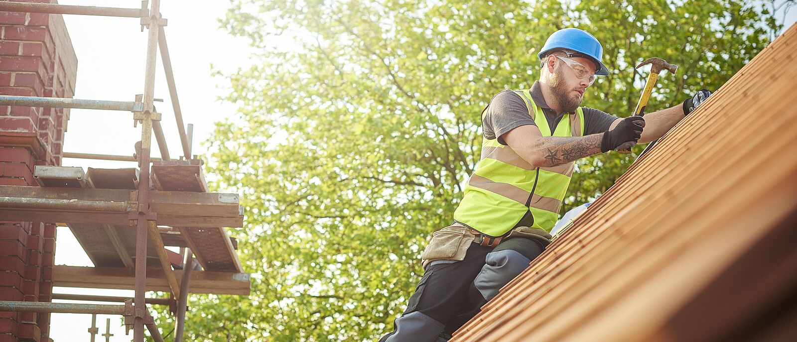 Auf einem Ziegeldach führt ein Handwerker Reparaturen aus.