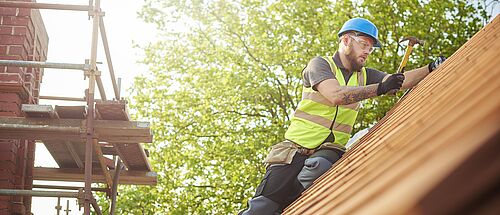 Auf einem Ziegeldach führt ein Handwerker Reparaturen aus.
