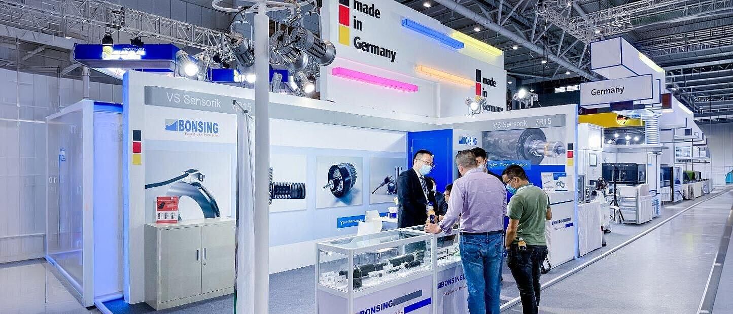 German Pavilion auf der Schleif- und Werkzeugbautechnologiemesse "Grinding Technology" in Japan vom 10.-12. März 2027 blick auf einen Messestand der German Pavilion an dem gerade zwei interessiert sich mit den Messestandvertreter unterhalten.