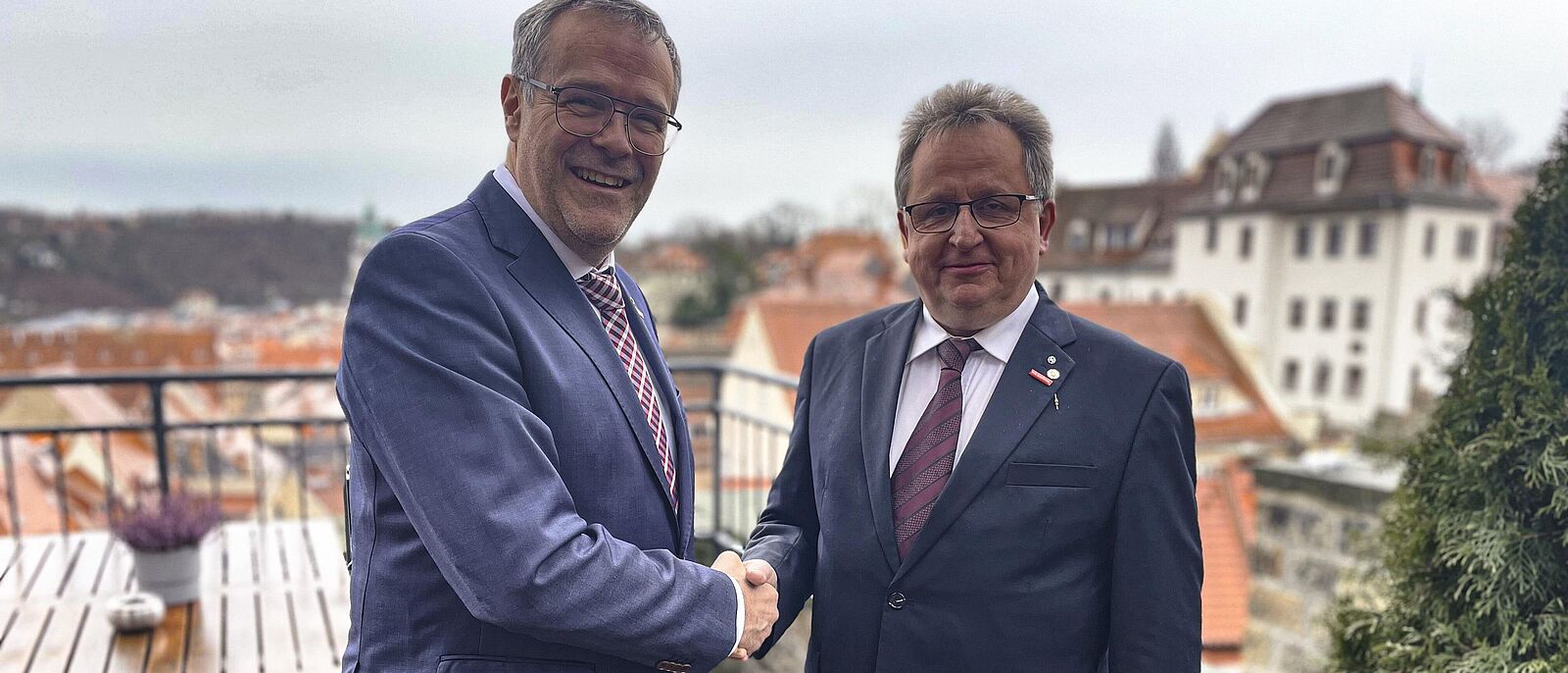 Jörg Dittrich gratuliert Peter Liebe- sie stehen auf einem Balkon mit Blick auf Hausdächer.