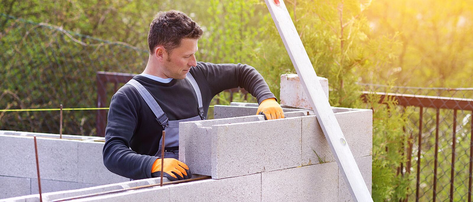 Baustelle - eine Person in einem Rohbau eines Hauses und mauert mit einer Maurerkelle aus Steinen eine Wand.