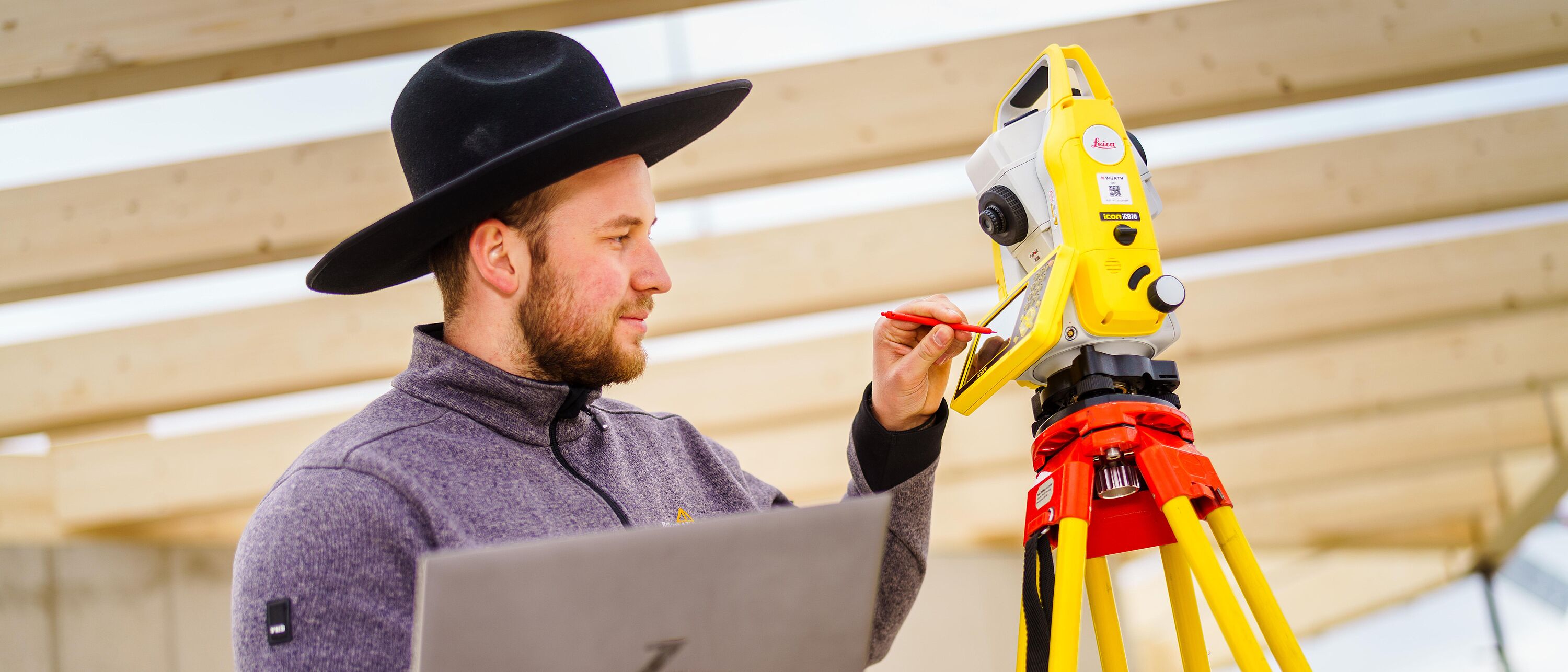 Eine Person mit einem Zimmerer-Hut benutzt ein modernes Tachymeter zum Ein- und Aufmessen auf der Baustelle.