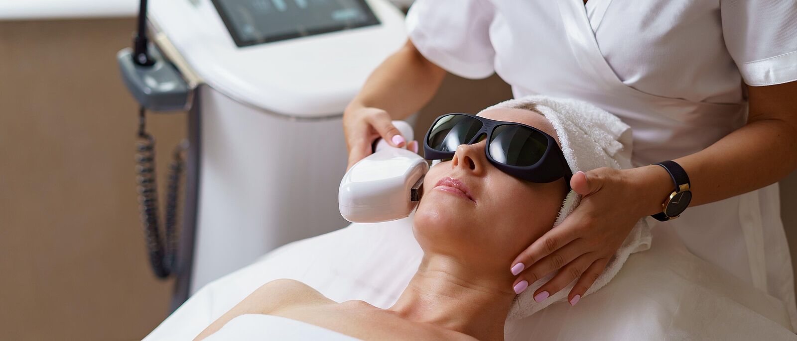 Blick auf eine Kosmetikerin die eine liegende Kundin mit Schutzbrille einem Anti-Aging-Verfahren unterzieht.