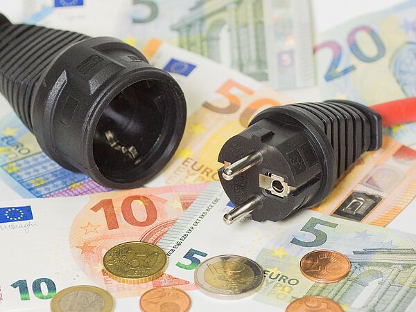 Makroaufnahme von Geldscheinen und Münzen, die auf einem Tisch liegen darauf eine Stromkabel mit Stecker.