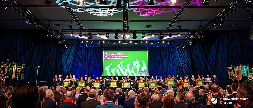 Gruppenbild  © alle geladenen Meister stehen mit ihren Meisterbriefen und einem Blumenstrauß auf der Bühne. Im Hintergrund Lichteffekte.