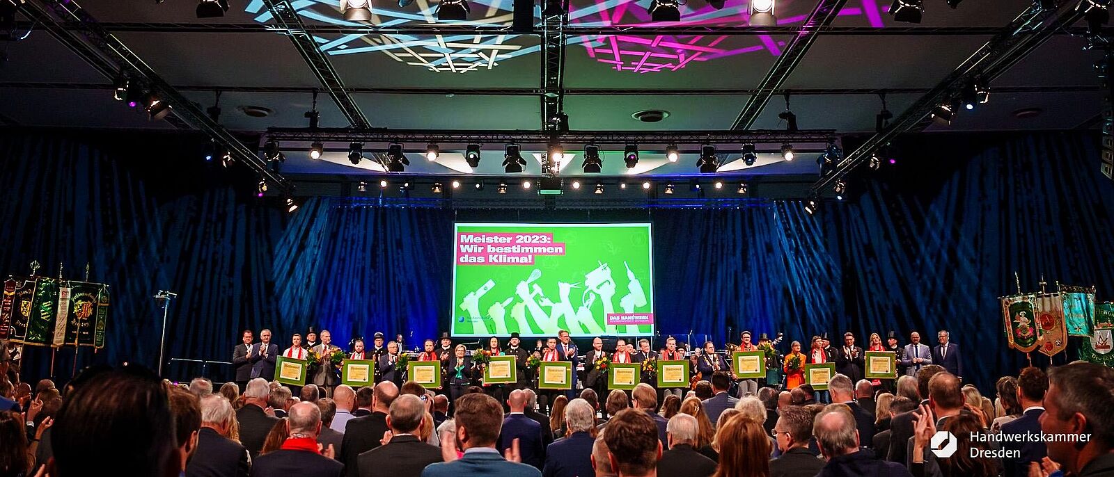 Gruppenbild  © alle geladenen Meister stehen mit ihren Meisterbriefen und einem Blumenstrauß auf der Bühne. Im Hintergrund Lichteffekte.