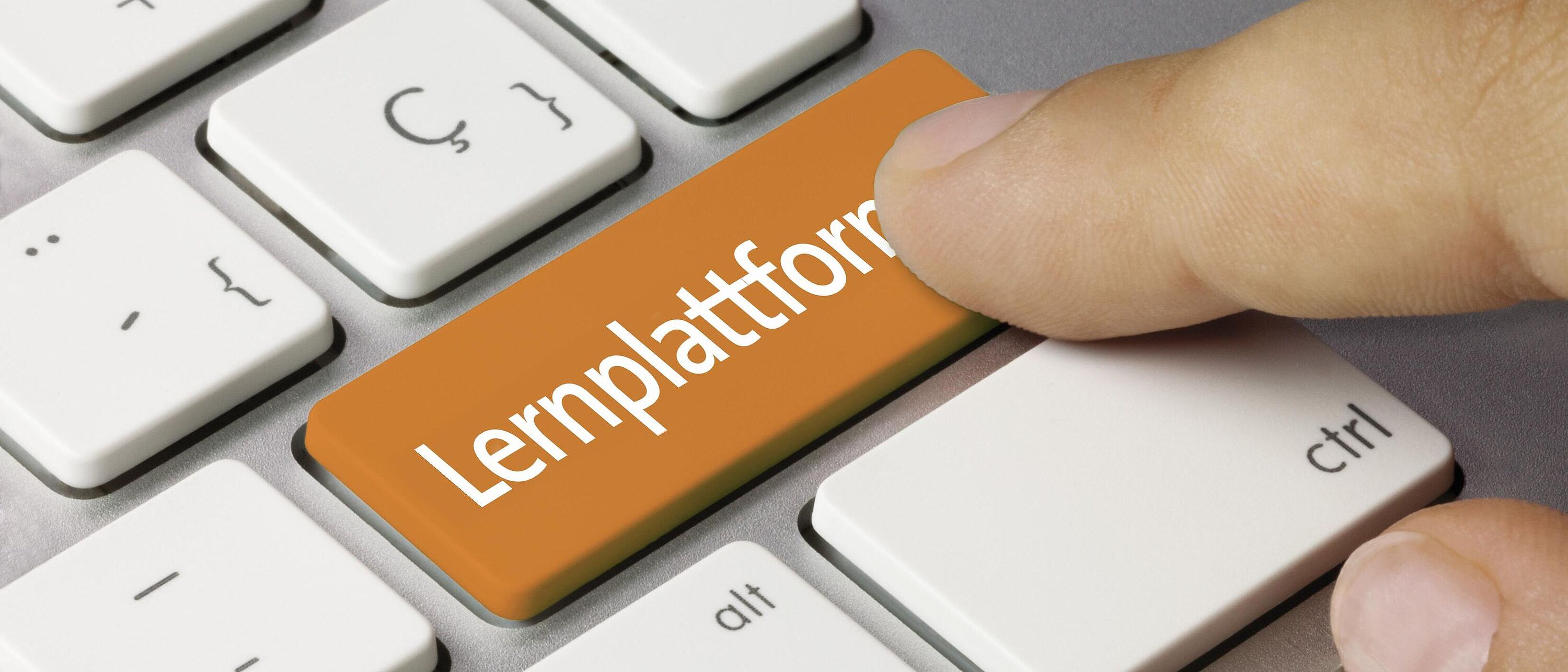 Macroaufnahme einer Tastatur, auf der Eingabetaste der weiße Schriftzug auf orangenen Hintergrund \"Lernplattform\". Darüber ein Zeigefinger der die Taste drücken will.