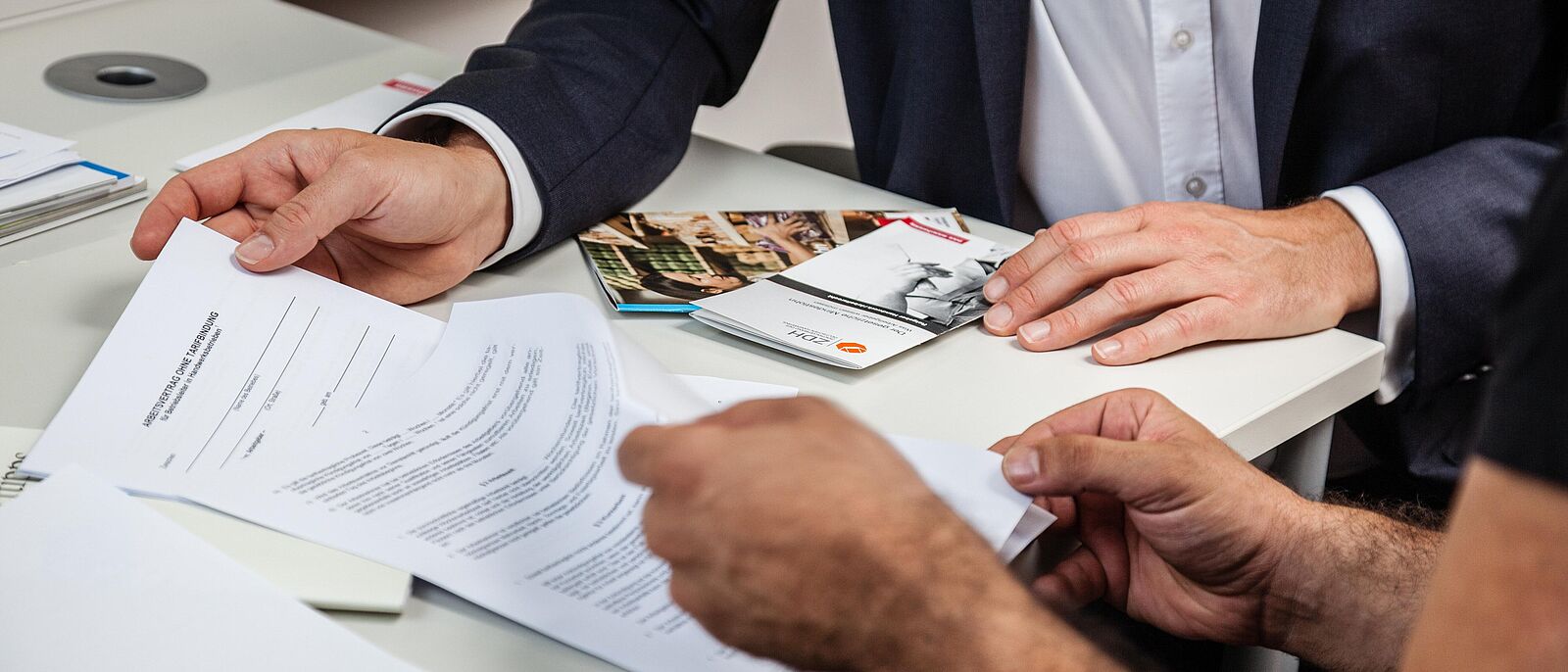 Zwei Personen sitzen nebeneinander und schauen prüfend in vor sich liegenden Dokumente und Formulare und sprechen dazu.