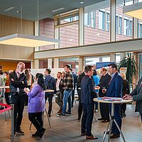 Im Foyer von njumii - Menschen stehen an Tischen oder im Raum begrüßen sich oder unterhalten sich