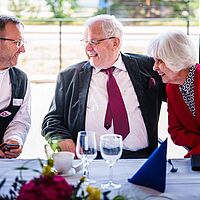 Drei Personen sitzen am tisch und unterhalten sich begeistert