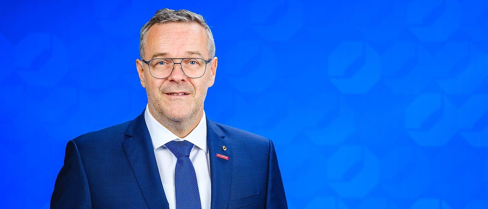 Dachdeckermeister Jörg Dittrich, Präsident der Handwerkskammer Dresden steht vor einer blauen Logo-Wand der Handwerkskammer Dresden