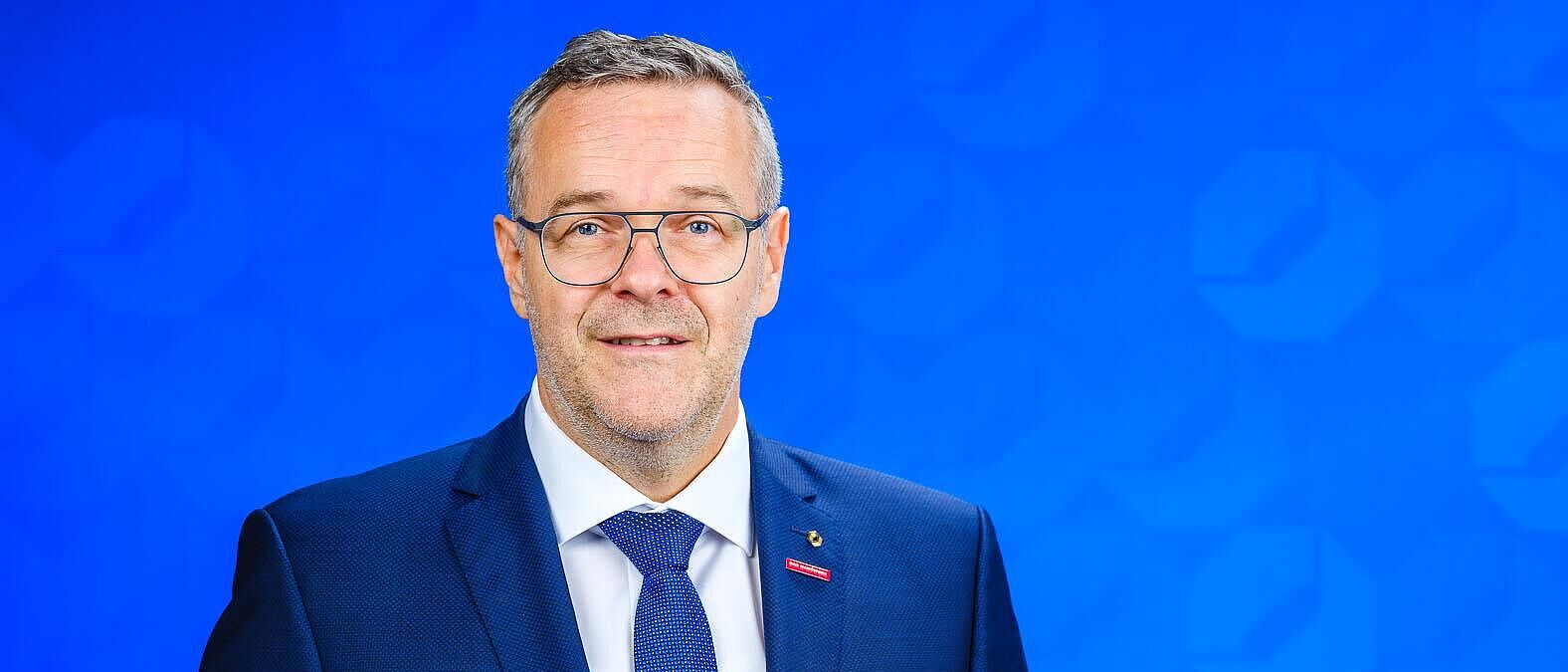 Dachdeckermeister Jörg Dittrich, Präsident der Handwerkskammer Dresden steht vor einer blauen Logo-Wand der Handwerkskammer Dresden