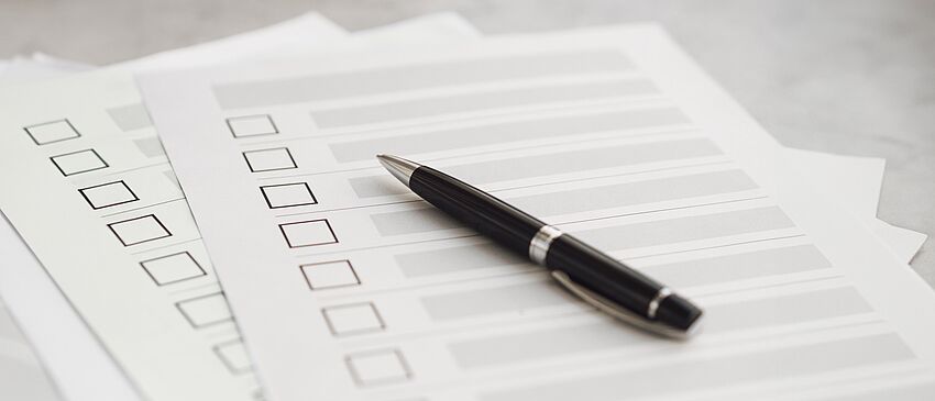 Fragebögen für Multiple-Choice-Fragen liegen zusammen mit einem schwarzem Kugelschreiber auf einem Tisch.