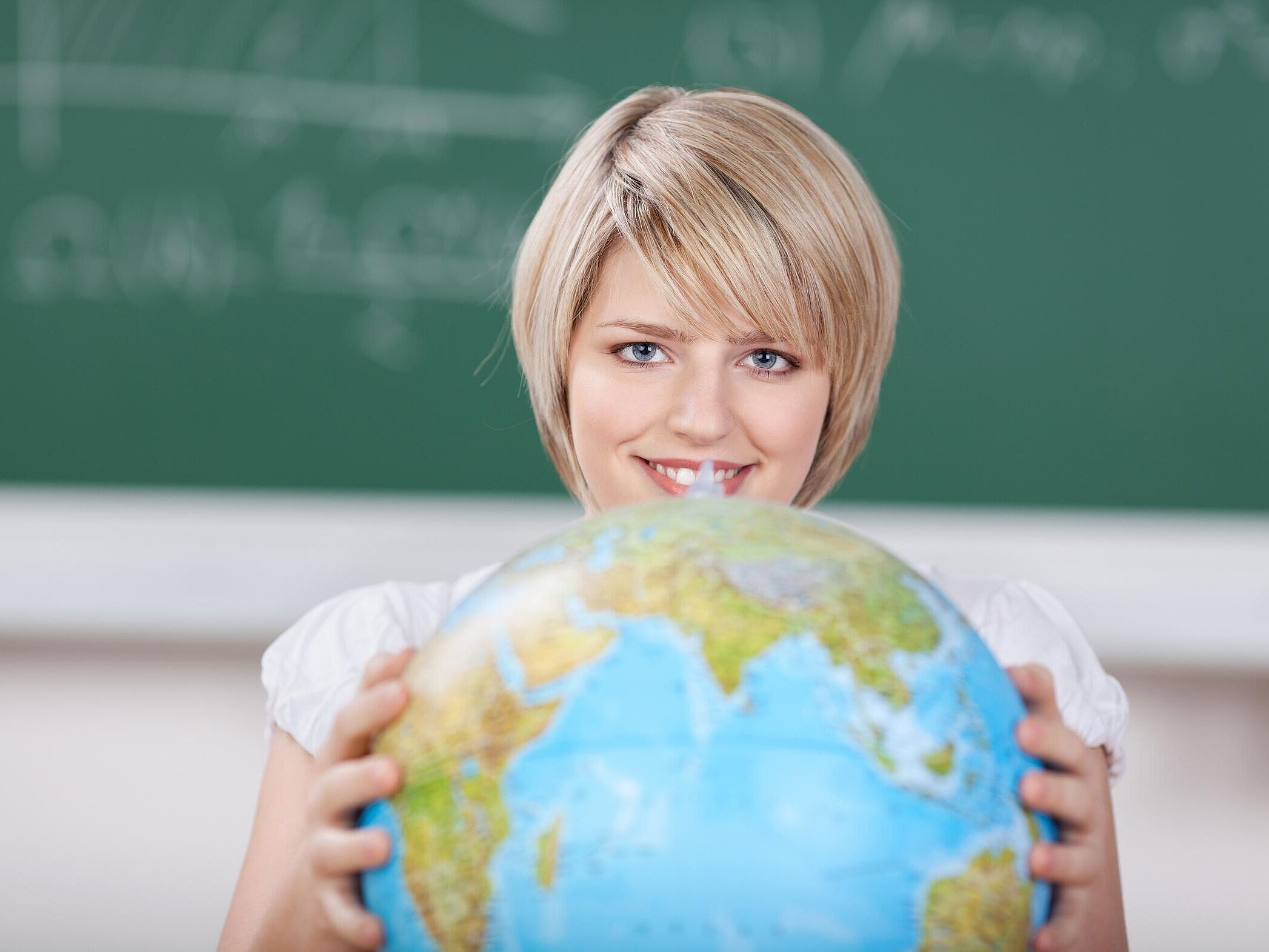 Person befindet sich in einem Klassenzimmer und dreht einen Globus