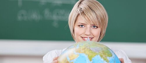 Person befindet sich in einem Klassenzimmer und dreht einen Globus