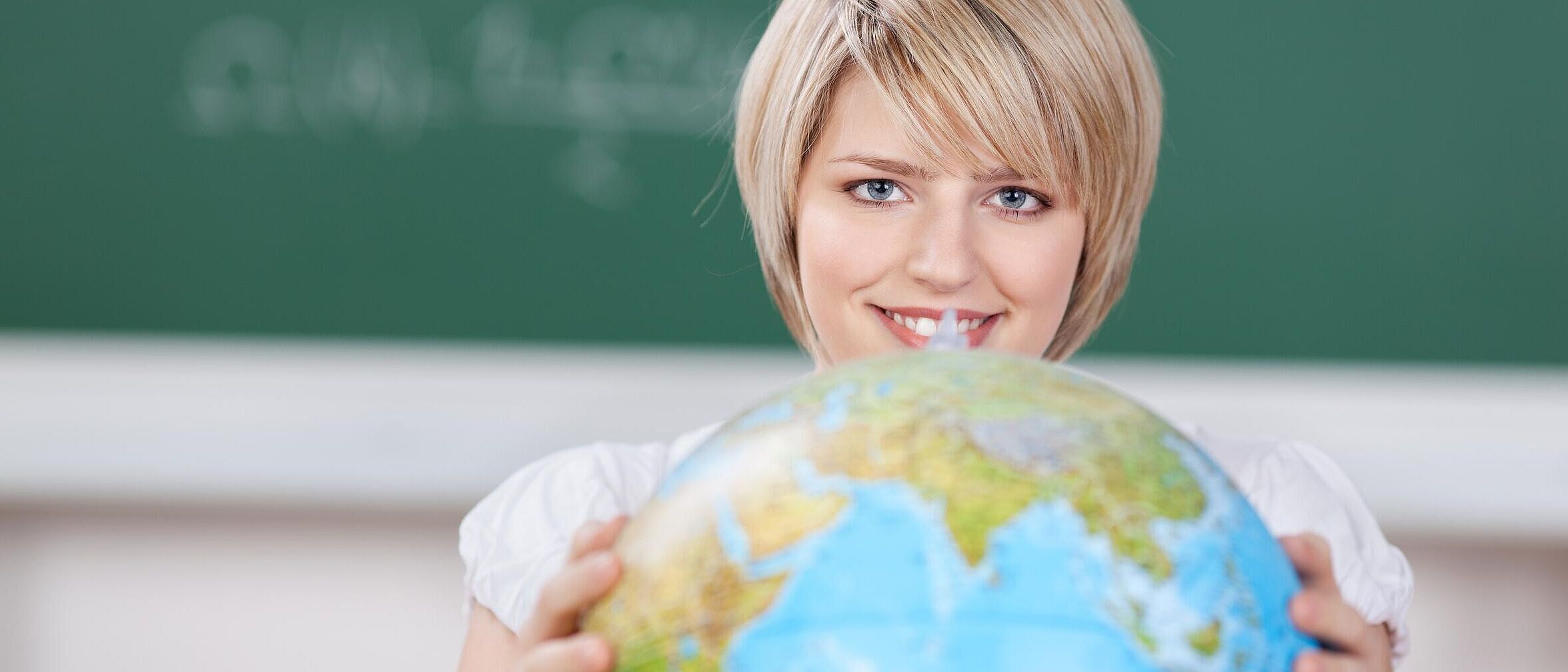 Person befindet sich in einem Klassenzimmer und dreht einen Globus