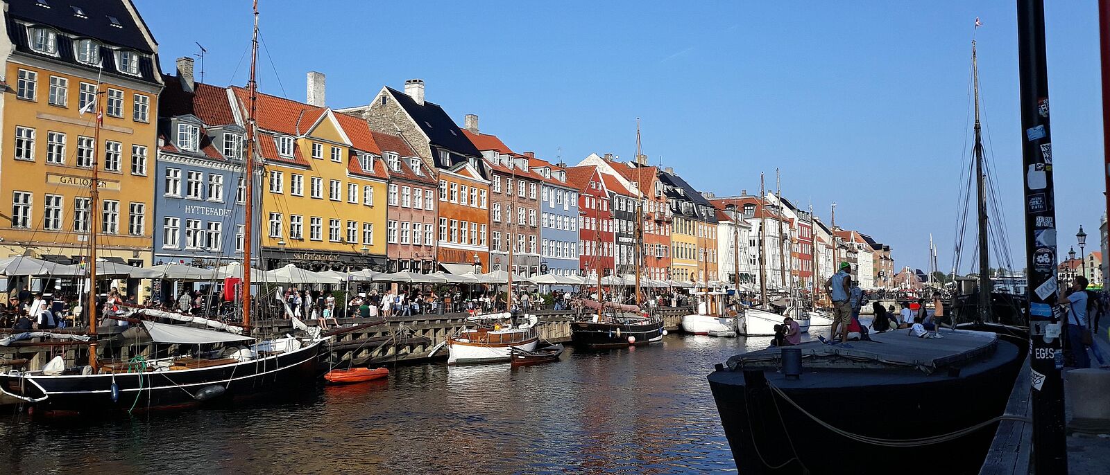 Blick auf die Uferpromenade mit den bunten Häusern von Kopenhagen, im Vordergrund der Fluß mit verschiedenen größeren und kleineren Booten.
