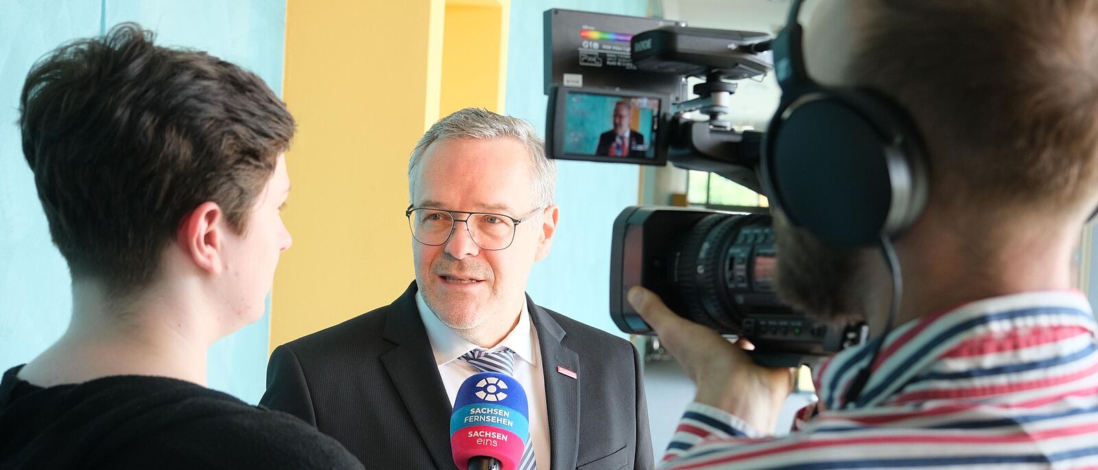 Präsident der Handwerkskammer Dresden, Jörg Dittrich gibt einem Fernsehteam gerade ein Interview. Vor dem Präsidenten stehen ein Kameramann und ein Journalist, die ihm in diesem Moment Fragen stellen, auf die der Präsident antwortet.