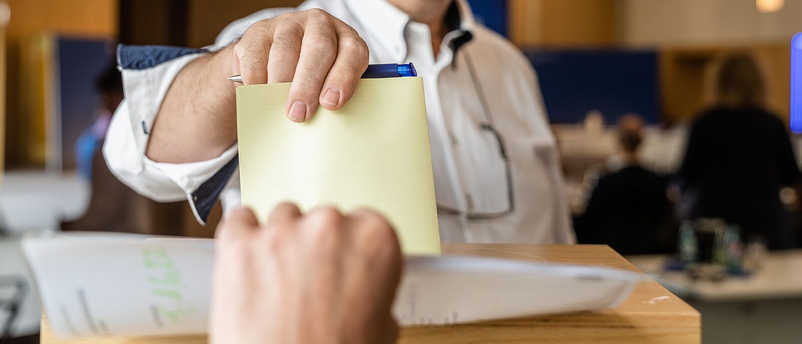 Eine Person steht vor einer Wahlurne und wirft seinen Wahlzettel ein.