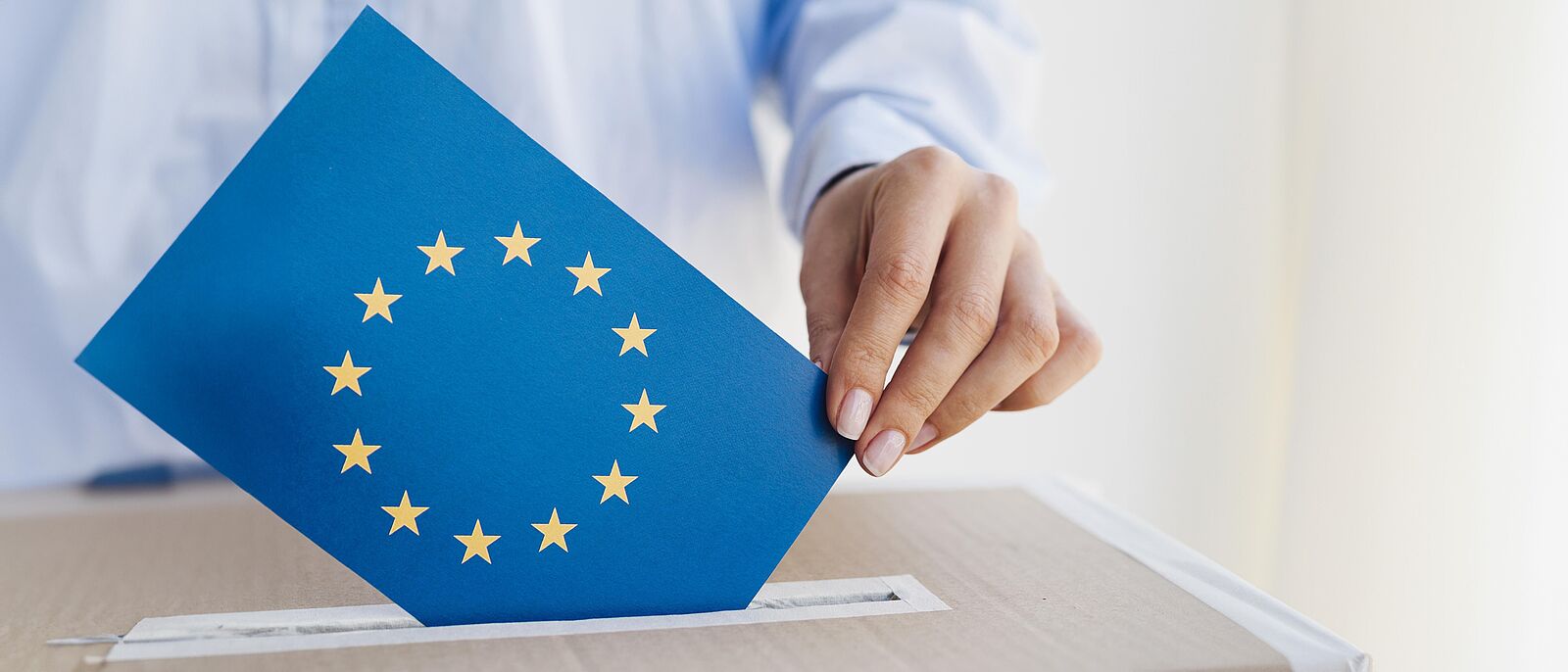 Eine weibliche Person legt einen Umschlag der Europäischen Union in eine Wahlbox.