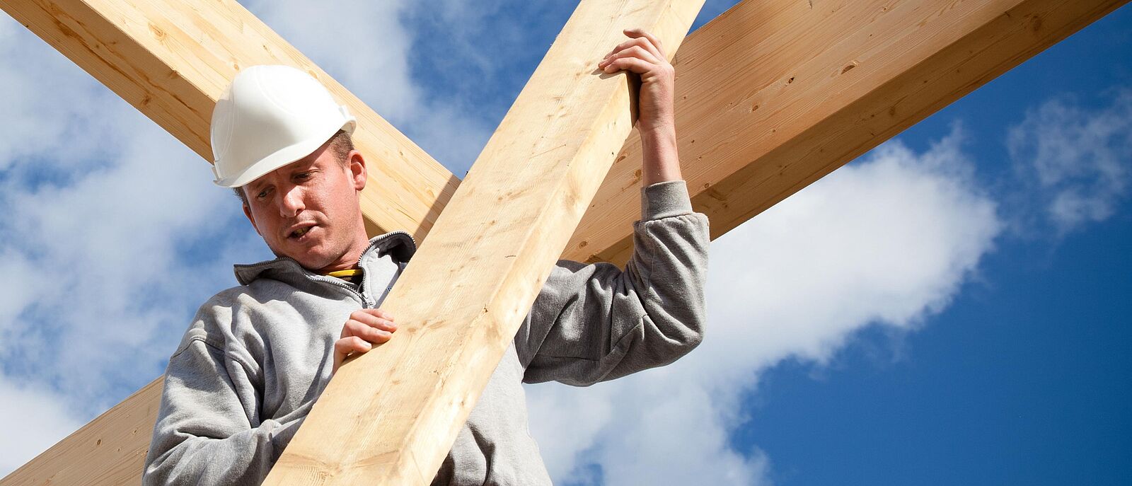 Eine Person in Dachdeckerberufsbekleidung positioniert gerade eine Holzleiste am einem Dachstuhl aus Holz.