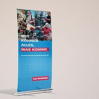Roll-Up mit dem Imagekampagnenspruch \" Wir können alles was kommt.\" auf blauem Hintergrund. Im oberen Bereich 9 Berufs-Portraits (Konditor, Zimmermann, Metallbauer, Augenooptiker, Elektrotechniker, Bau und Ausbau, Landmaschinenmechaniker, Fleischer).