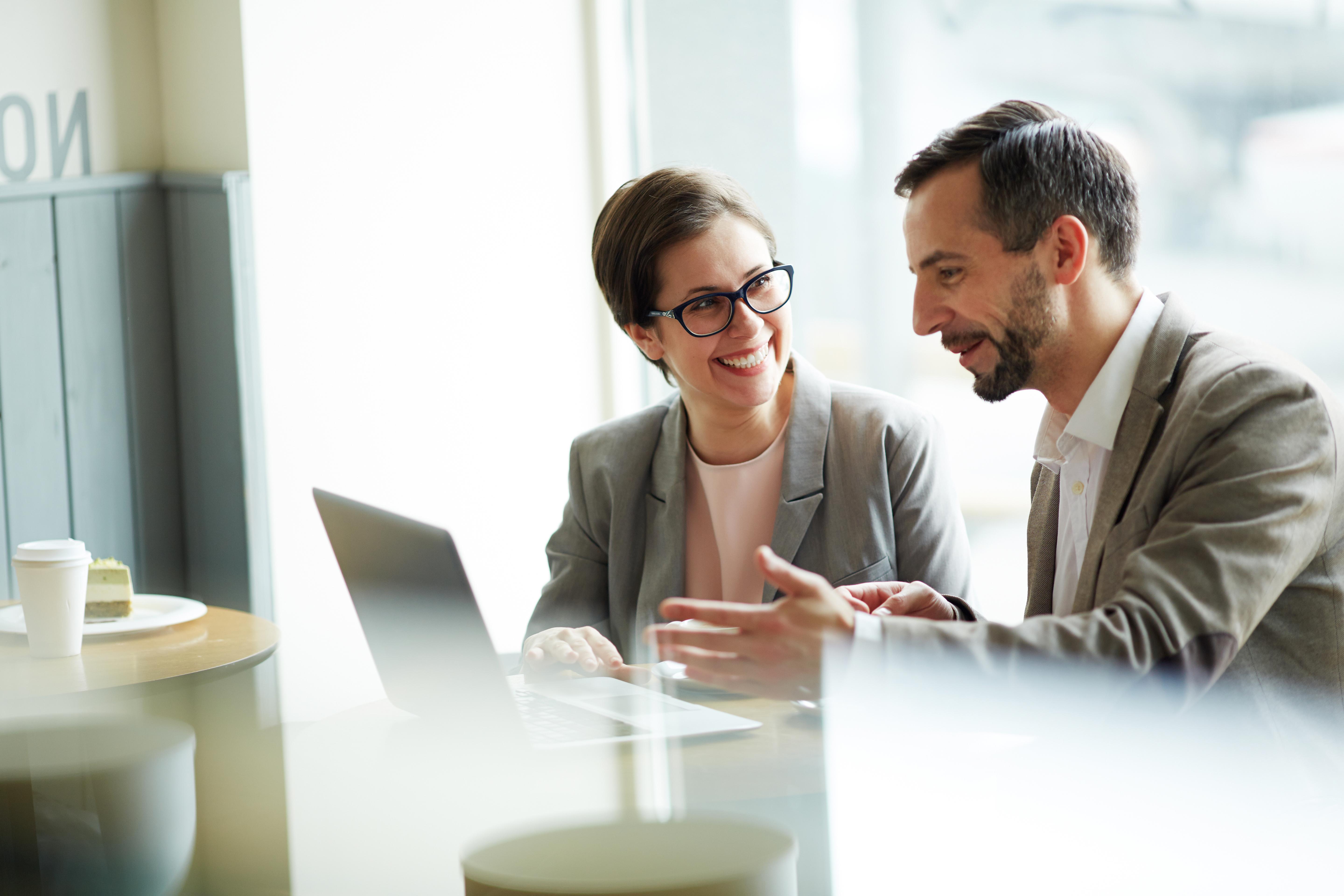zwei Personen sitzen am Laptop und arbeiten und lachen