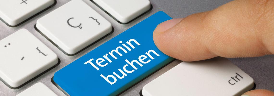 Makroaufnahme einer Tastatur, auf der Eingabetaste steht \"Termin buchen\" welche gerade von einer Person betätigt wird.